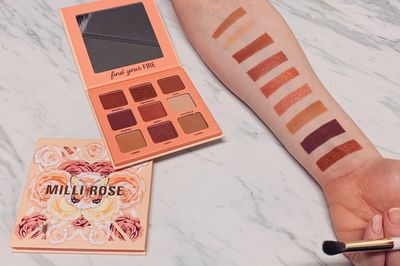 a girl holds out her arm displaying 9 warm eyeshadow swatches next to a MILLI ROSE palette