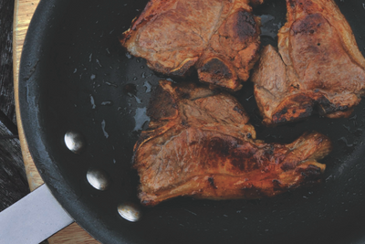 Three steaks sizzle in a pan