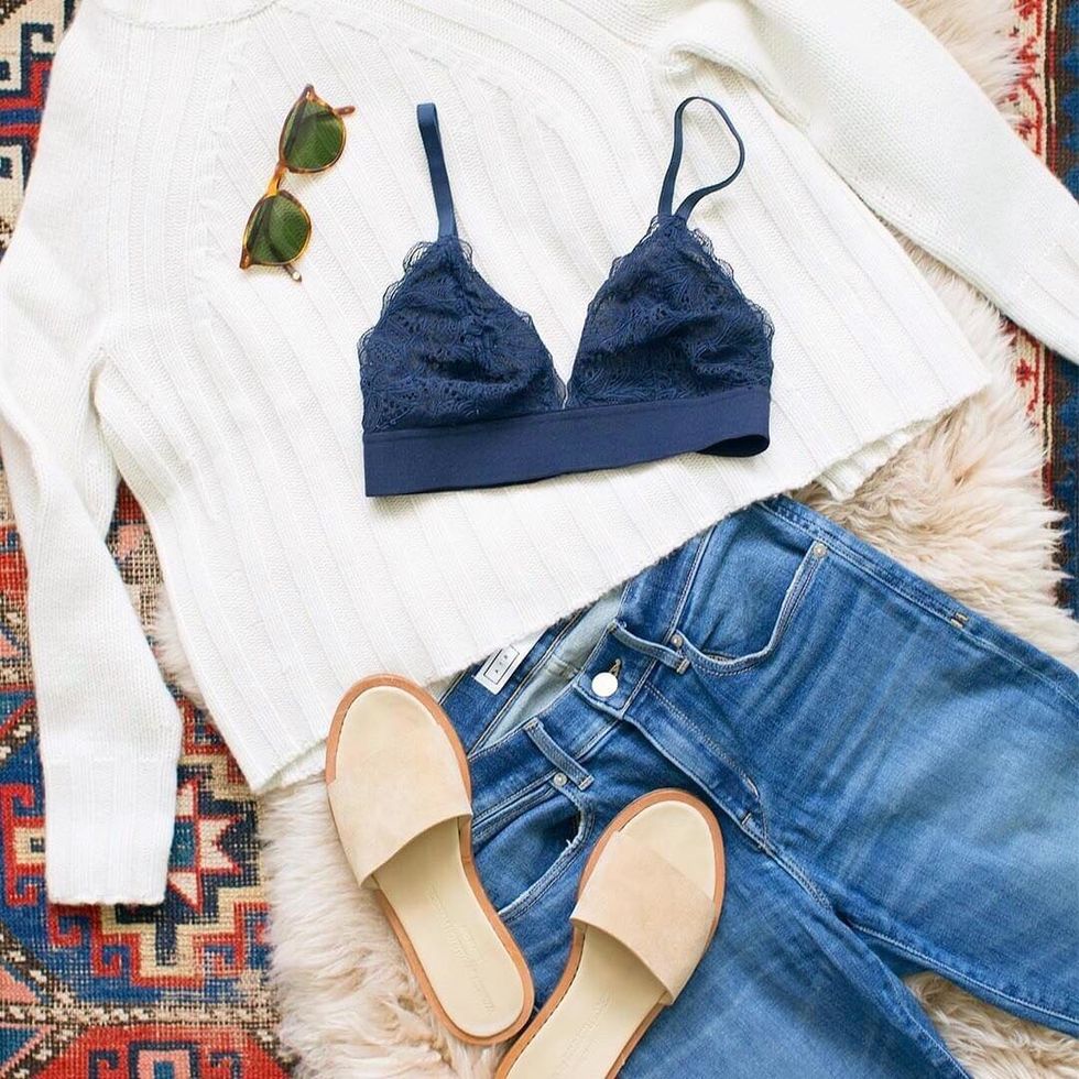white sweater and a navy blue bralette are layed out on an aztec rug